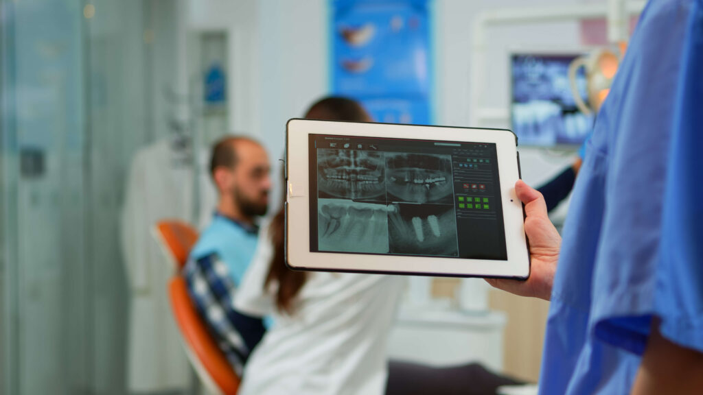 close-up-dentist-nurse-holding-tablet-with-digital-radiography-while-doctor-is-working-with-patient-background-examining-teeth-problem-sitting-stomatological-chair-dental-clinic (1)
